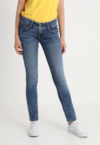 Jeans skinny in denim blu medio con scoloriture, design a cinque tasche, chiusura con zip e doppio bottone. Abbinati a sneaker bianche.