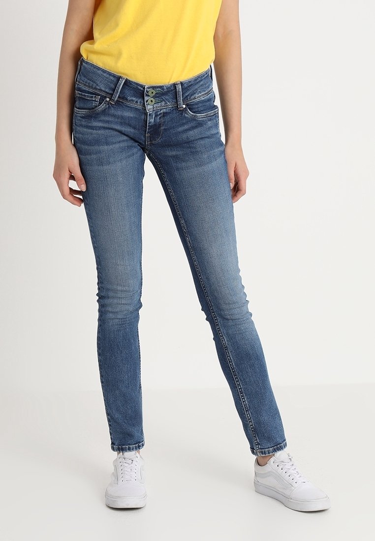 Jeans skinny in denim blu medio con scoloriture, design a cinque tasche, chiusura con zip e doppio bottone. Abbinati a sneaker bianche.