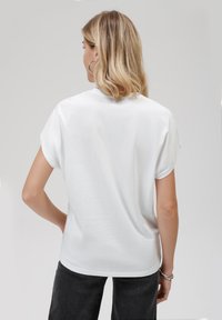 T-shirt blanc à manches courtes avec un col rond, texture lisse et coupe décontractée, présenté de dos avec un design uni.