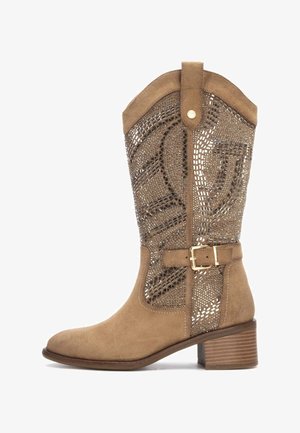 Bota de ante hasta la rodilla en color marrón con un patrón de cortes decorativos, acento de hebilla y tacón de tipo apilado. Textura suave con un diseño estructurado.