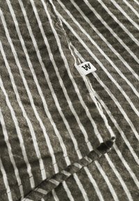 Striped fabric in olive green and white, featuring a textured, slightly crinkled surface. A small tag with the letter "A" is visible.