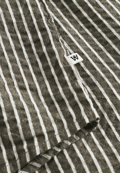 Tissu rayé en vert olive et blanc, présentant une surface texturée légèrement froissée. Une petite étiquette avec la lettre "A" est visible.