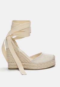 Beige espadrille kile-sko med en vævet jutesål, stofoverdel og lange stofbånd til ankel-lukning. Flad hæl og åben tå-design.
