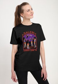 Schwarzes T-Shirt mit einer Retro-Illustration von fünf Charakteren in orangefarbenen Shorts, vor einem lila Hintergrund, mit dem Text "Salem Summer Camp '78".