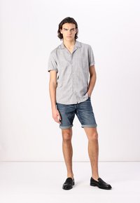 Chemise grise à manches courtes avec boutons en tissu léger, associée à un short en denim roulé et des mocassins noirs. Design simple, coupe décontractée.