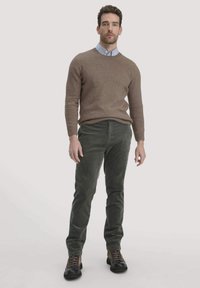 Bruine trui, lichtblauw overhemd met kraag, groene ribstof broek en donkerbruine laarzen. Glad textiel met een aansluitend ontwerp.