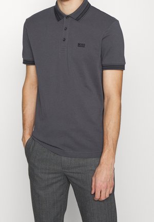 Mand iført en mørkegrå Hugo Boss poloshirt med sortstribet krave og ærmekanter, kombineret med grå mønstrede bukser.