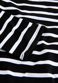 Mustvalge triibuline kangas, millel on sile tekstuur. Omaduseks ühtlased horisontaalsed triibud, lihtsa õmmeldud ääre ja manseti detailiga.