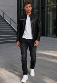 Junger Mann, der draußen läuft, trägt eine schwarze Lederjacke, ein weißes T-Shirt, schwarze Jeans und weiße Sneakers in der Nähe von Betontreppen.