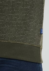 Olijfgroene sweatshirt van structuurstof, met witte horizontale strepen, geribbelde manchetten en een blauwe label op de onderste zoom.