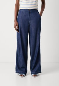 Weite Jean-Pants in Dunkelblau mit Knopfverschluss und Vorderentaschen. Glatte Textur mit kontrastierenden Nähdetails.