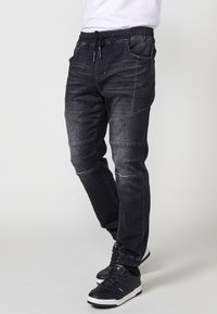 Pantalones jogger de mezclilla negra con cintura elástica y cordón ajustable, que cuentan con bolsillos laterales y detalles de costura texturizada en las piernas.