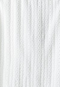 Tessuto bianco con righe verticali di piccoli ricami ad occhio ovale che creano una superficie texturizzata e patternizzata.