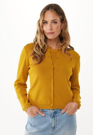Mustard yellow cardigan with long sleeves, ribbed texture, scalloped edges, and round buttons, paired with light blue high-waisted jeans.
