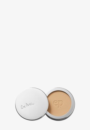 Boîtier rond et compact contenant une poudre crème beige clair, extérieur métallique argenté avec logo embossé, texture lisse à l'intérieur, design à ouverture par clapet.