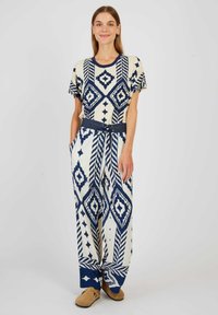 Jumpsuit en coton crème avec des motifs géométriques navy. Manches courtes, taille élastique, poches latérales et coupe décontractée.
