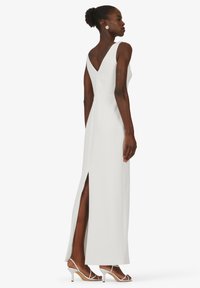 Langes weißes Kleid mit V-Ausschnitt und seitlichem Schlitz. Glatter Stoff, maßgeschneiderter Schnitt und kombiniert mit weißen Riemchen-Highheels.