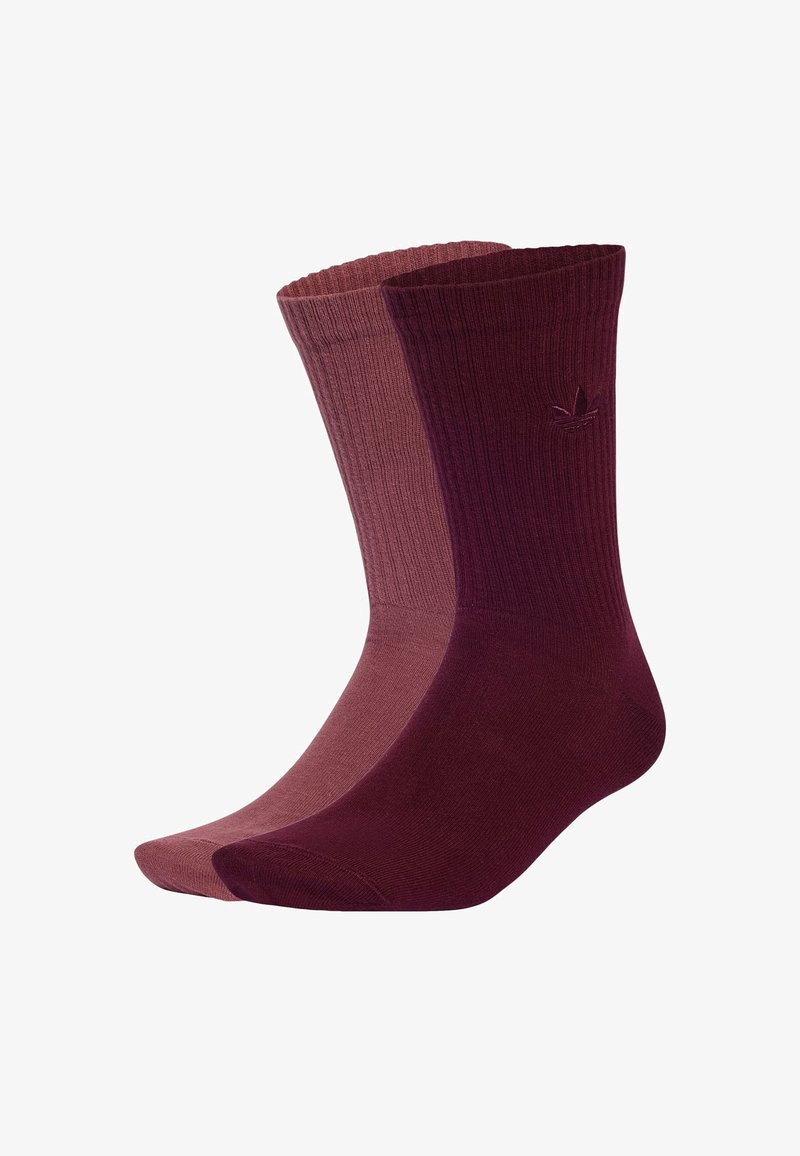 Paar gerippte Crew-Socken, eine dunkelbordeaux mit gesticktem Logo, die andere in staubigem Rosa, nebeneinander auf weißem Hintergrund dargestellt.