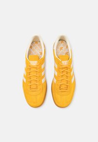 Kollane nahast tennisekingad valgete triipudega, tekstureeritud viimistlusega ja pehmendatud keelega. Siseosas on korduv logo muster ja pehmendusega sisetald.