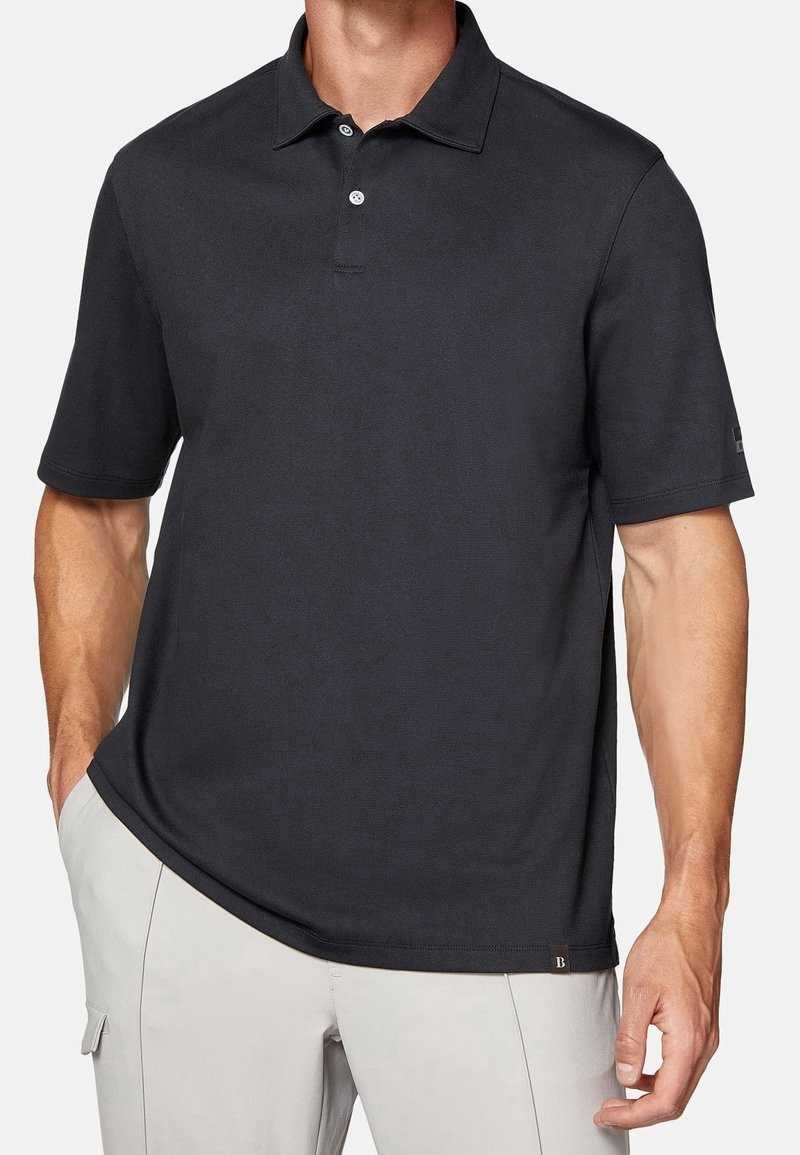 Polo noir avec col, manches courtes et patte de boutonnage à deux boutons. Fabriqué en tissu texturé, avec une petite étiquette de marque sur l'ourlet.