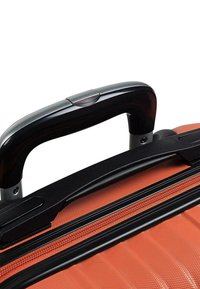 Maleta rígida de color naranja texturizado, con un asa retráctil negra y detalles en cremallera contrastantes.