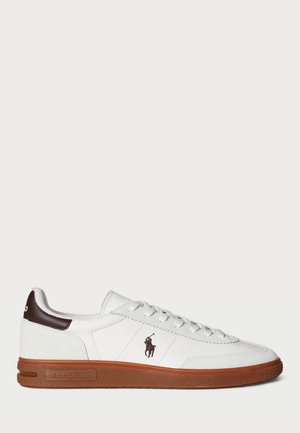 Białe niskie sneakersy z brązową gumową podeszwą, wiązane i z ciemnobrązowym logo gracza polo po boku i na pasku z tyłu.