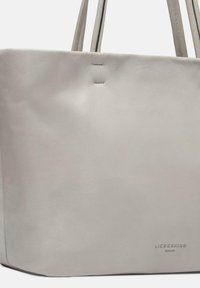 Hellgraue Leder-Tote-Tasche mit minimalistischem Design, ausgestattet mit einer glatten Textur und subtiler Markenkennung am Boden. Inklusive doppelter Schulterträger.