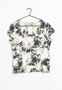 Sort og hvid blomstret blouse med korte ærmer, en rund halsudskæring og en samlet kant, hængende på en sort bøjle.