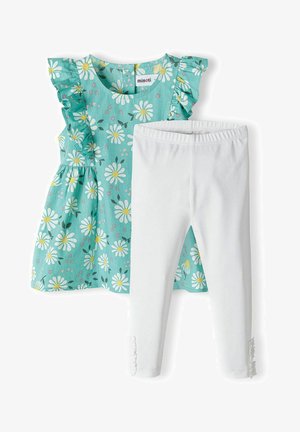 Egy két részes szett, amely egy világoskék toppból áll, fehér margaréta mintával és fodros ujjakkal, fehér leggingsszel, fodros díszítéssel párosítva.