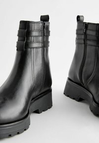 Bottes noires en cuir jusqu'à la cheville avec une finition lisse, des zips latéraux structurés et une semelle en caoutchouc épaisse dotée d'une rainure texturée.