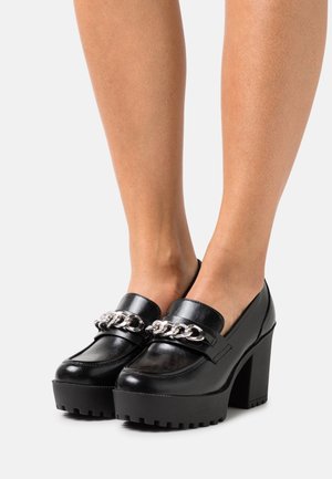 Chaussures en cuir noir avec une plateforme épaisse et un talon bloc haut. Présentent un accent en chaîne argentée sur le devant et une texture lisse.
