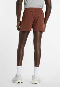 Pantalones cortos deportivos marrones hechos de tela ligera, con una cintura elástica y un pequeño bolsillo con cremallera en la parte trasera.