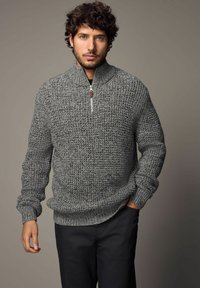 Grå zip-neck sweater med et struktureret, chunky strikmønster samt ribbede håndled og kant, parret med mørke bukser.