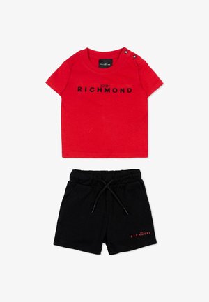 Chemise rouge à manches courtes avec le texte « John Richmond » et short noir à cordon avec logo rouge « Richmond » assorti sur la jambe gauche.