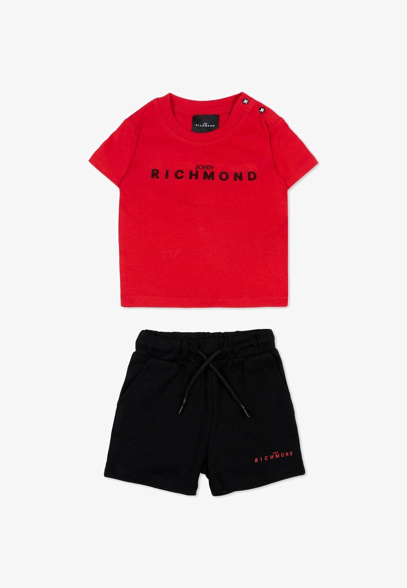 Chemise rouge à manches courtes avec le texte « John Richmond » et short noir à cordon avec logo rouge « Richmond » assorti sur la jambe gauche.