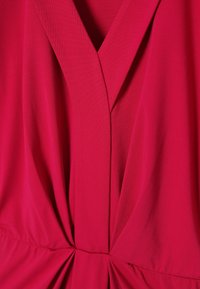 Rotes Kleid mit V-Ausschnitt, gerafftem Stoffdetail in der Taille und glatter Textur. Das Material scheint leicht und fällt elegant.