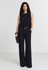 Top court noir à coupe droite, associé à un pantalon large noir taille haute avec des accents de boutons et des poches latérales.