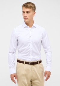 Witte lange mouwen shirt met een klassieke kraag, knoopsluiting en een getailleerde snit, gecombineerd met lichtbeige broek en een bruine riem.