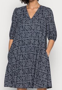 Marinblå klänning med V-hals, trekvarts puffärmar, fickor och ett vitt paisley-mönster. Tillverkad av lätt material med en avslappnad passform.