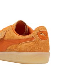 Sneaker arancioni in suede con una parte superiore testurizzata, dettagli in pelle liscia e una suola in gomma traslucida. Presenta un logo sul tallone.