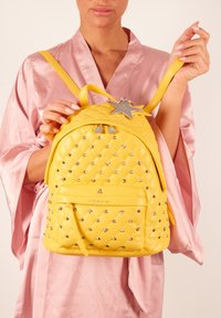Geel gewatteerde rugzak met zilveren steraccenten en hardware. Beschikt over een voorkantvak en verstelbare schouderbanden. Glad, glanzend oppervlak.