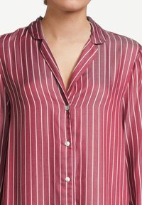 Camicia a maniche lunghe a righe rosse con colletto, caratterizzata da righe verticali bianche e bottoncini piccoli. Il materiale sembra leggero e trasparente.
