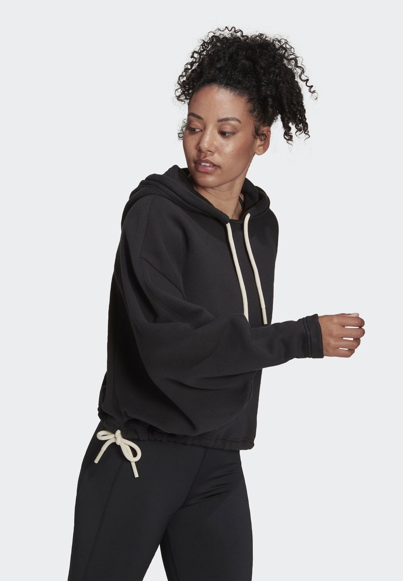 Hoodie nero corto con cappuccio regolabile, maniche ampie e vestibilità morbida, abbinato a leggings neri. Tessuto morbido e design semplice.