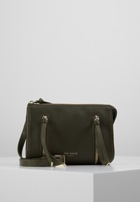 Borsa a tracolla in pelle verde oliva con hardware dorato, due tasche con zip e tracolla regolabile. Texture liscia, design minimalista.