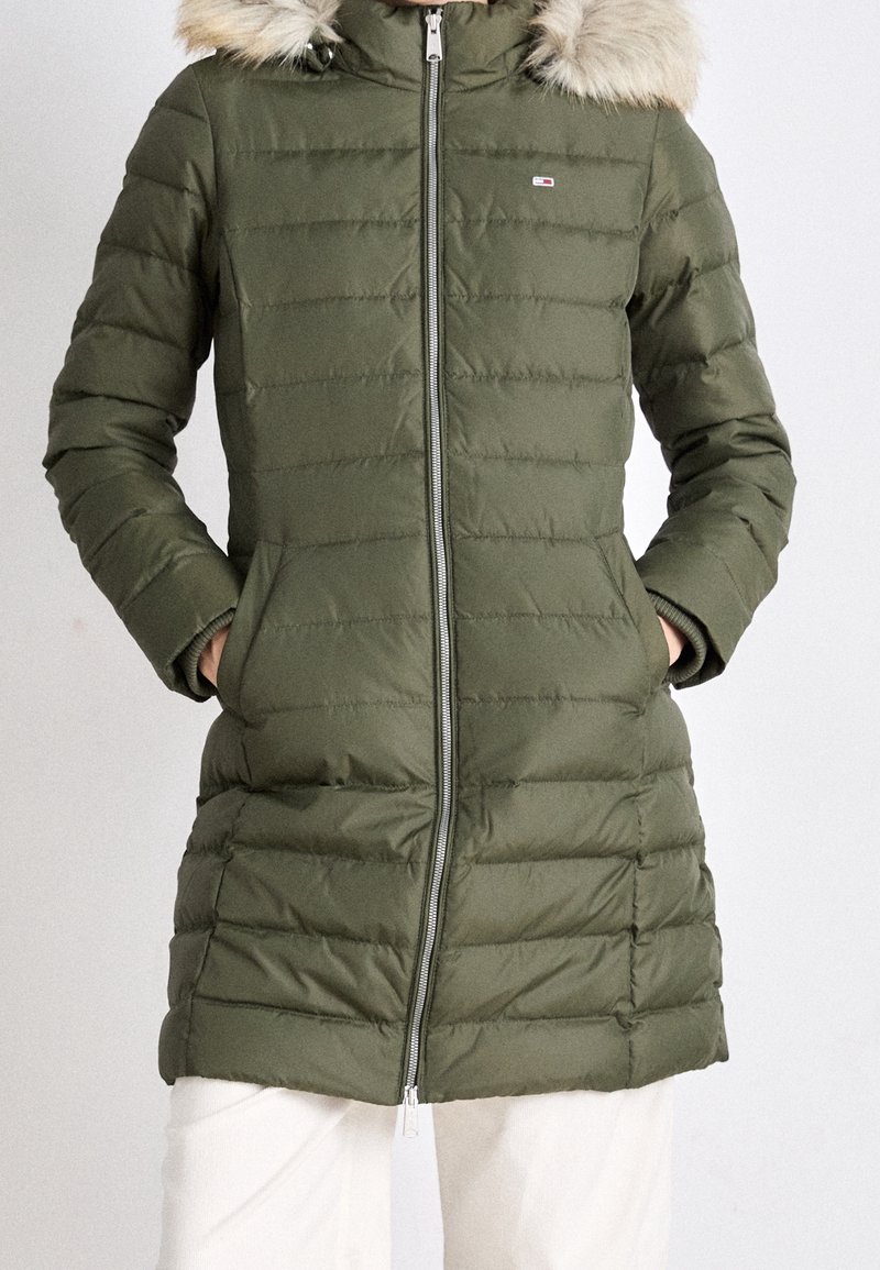 Olivgrüner Puffer-Mantel mit Kapuze aus Kunstpelz, gestepptem Design, Reißverschluss und seitlichen Taschen. Mit einem Logopatch auf der oberen Brust.