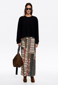 Suéter corto negro, falda larga de múltiples patrones en tonos beige, rojo y azul, bolso marrón y botines marrones. Gafas de sol cuadradas.