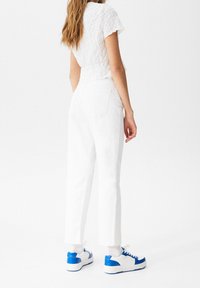 Haut blanc texturé court associé à un pantalon blanc taille haute. Baskets blanches et bleues avec des accents bleus et des semelles blanches complètent la tenue.