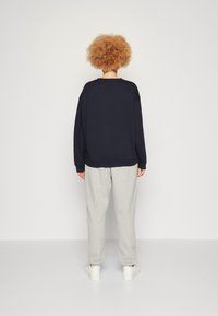 Felpa navy con spalle scese, abbinata a pantaloni della tuta grigi chiari. Tessuto morbido, vestibilità rilassata e sneakers bianche. Design semplice.