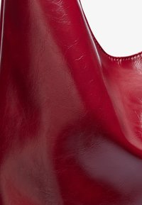 Borsa in pelle rossa con una texture liscia e lucida. Presenta un design morbido e un'apertura superiore curva, che mette in mostra un colore ricco e profondo.