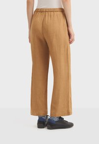 Pantalon large marron en tissu texturé avec taille élastique, porté avec des chaussures noires et des chaussettes bleues à pois.